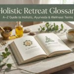 A serene book cover titled "Holistic Retreat Glossary: A–Z Guide to Holistic, Ayurveda & Wellness Terms." The image features an open book on a light wooden table surrounded by a mortar and pestle, eucalyptus leaves, herbal tea, and turmeric powder in soft, natural sunlight.